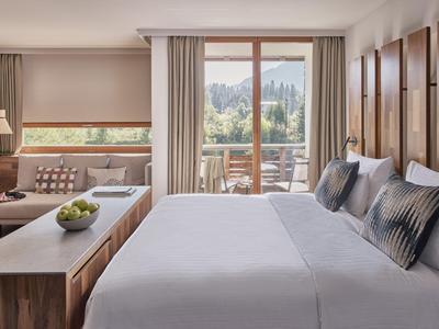 Helles Hotelzimmer mit Doppelbett, Sitzbereich und Blick auf Balkon mit grüner Landschaft.