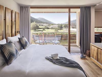 Modernes Hotelzimmer mit Doppelbett und Blick auf eine Terrasse und Berge.