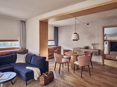 Modernes Wohnzimmer mit Holzfußboden, blauer Couch, Esstisch und großen Fenstern mit Ausblick.