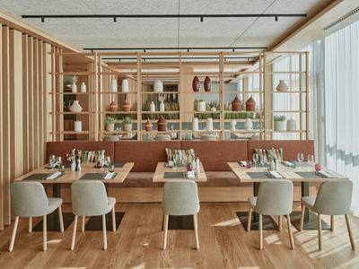 Modernes Restaurant mit Holzakzenten, bequemen Sesseln und großen Fenstern für viel Tageslicht.