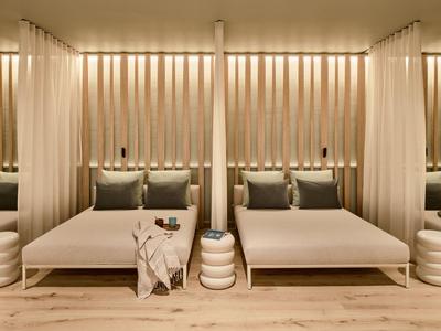 Modernes Hotelzimmer mit zwei großen Betten, beigen Vorhängen und warmem Holzfußboden.