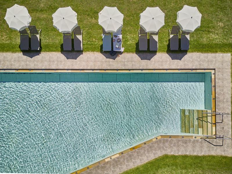 Pięć leżaków z białymi parasolami na zielonej trawie obok czystego basenu.