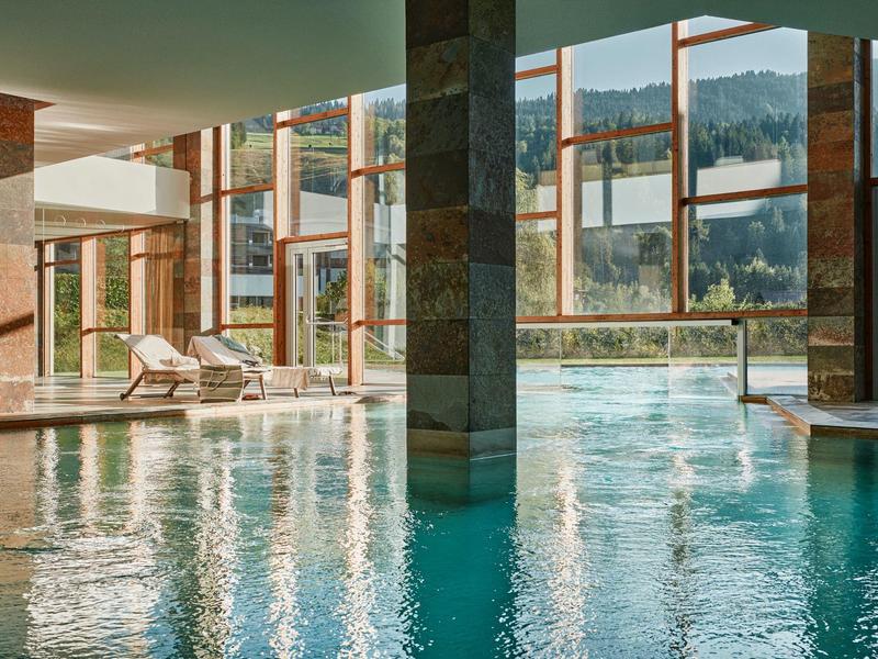 Basen kryty z dużymi oknami i widokiem na góry, leżaki po bokach.
