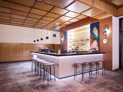 Area bar moderna in hotel con bancone illuminato, sgabelli e arte contemporanea al muro.