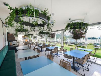 Ristorante luminoso e moderno con tavoli blu, piante sospese e vista su una terrazza.