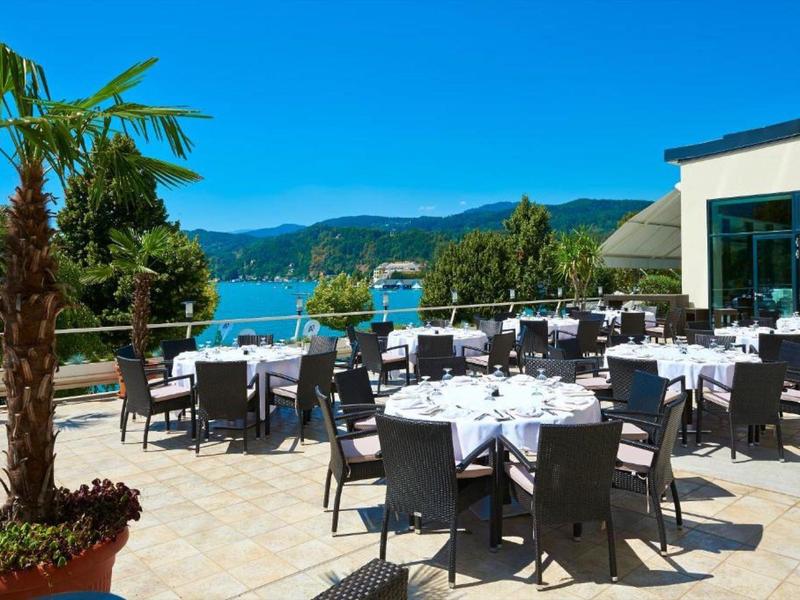 Terrazza con tavoli e sedie accanto a un hotel con vista su un lago e montagne.