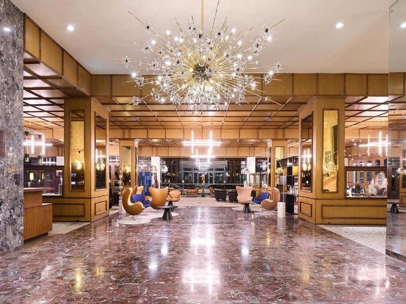 Ampio atrio dell'hotel con pavimento in marmo, poltrone moderne e grande lampadario.