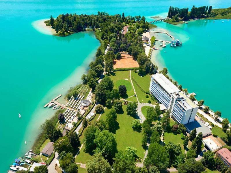 Vista aerea di una penisola verde con edifici di hotel e acqua turchese.