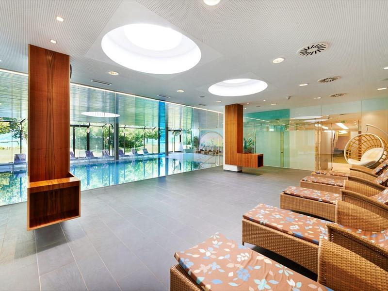 Area benessere moderna e luminosa con lettini e grandi finestre che danno su spazio verde.