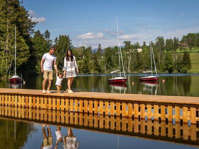 Una coppia cammina su un molo vicino al lago, circondata da alberi e due barche a vela.