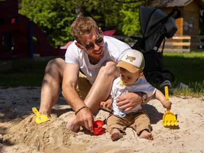 Vader en kind spelen samen in een zandbak buiten bij zonnig weer.