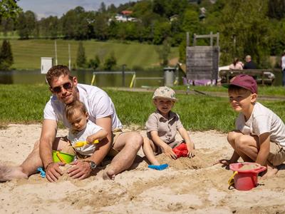 Padre che gioca con tre bambini in una sabbionaia in una giornata di sole al parco.