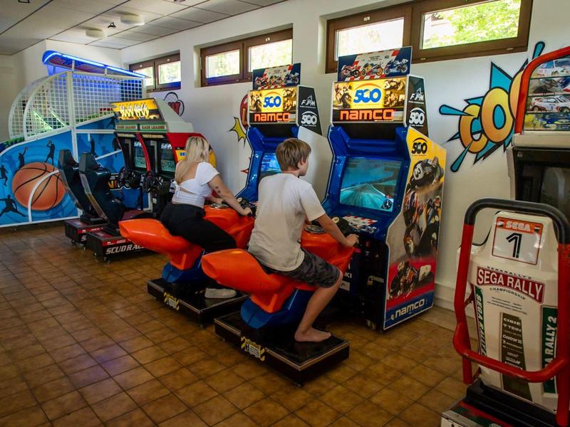 Een arcade speelruimte met basketbalspel, race-simulatoren en arcade machines in zonlicht.
