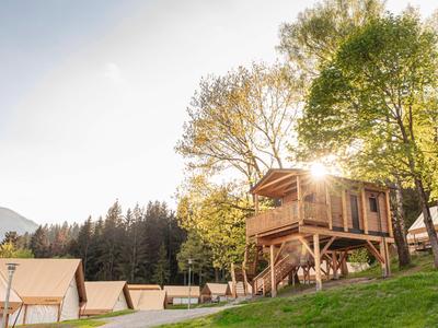 Casa del árbol de madera en una colina con vista a tiendas y árboles al atardecer