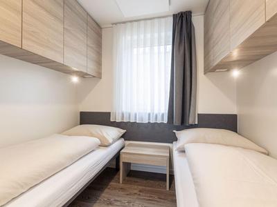 Habitación con dos camas individuales, armarios de madera y mesita bajo una ventana con cortinas blancas