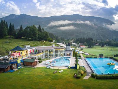 Bergresort mit Schwimmbädern, grünen Wiesen und bewaldeten Hügeln unter blauem Himmel.