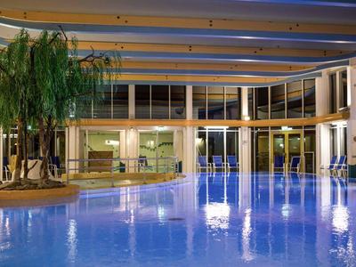 Hallenbad mit großem Becken, blauer Beleuchtung und Pflanzen auf heller, moderner Terrasse.