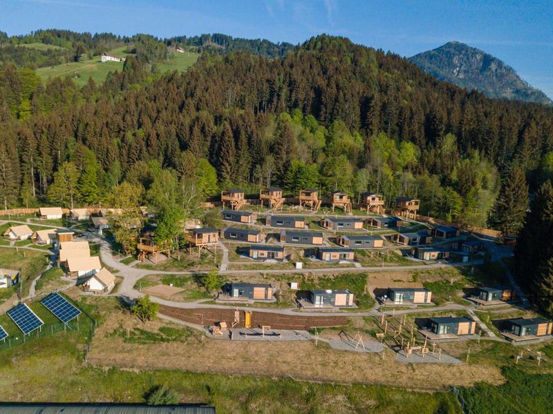 Moderne Einfamilienhäuser in Reihen mit großen Fenstern, umgeben von Wäldern und Bergen im Hintergrund.