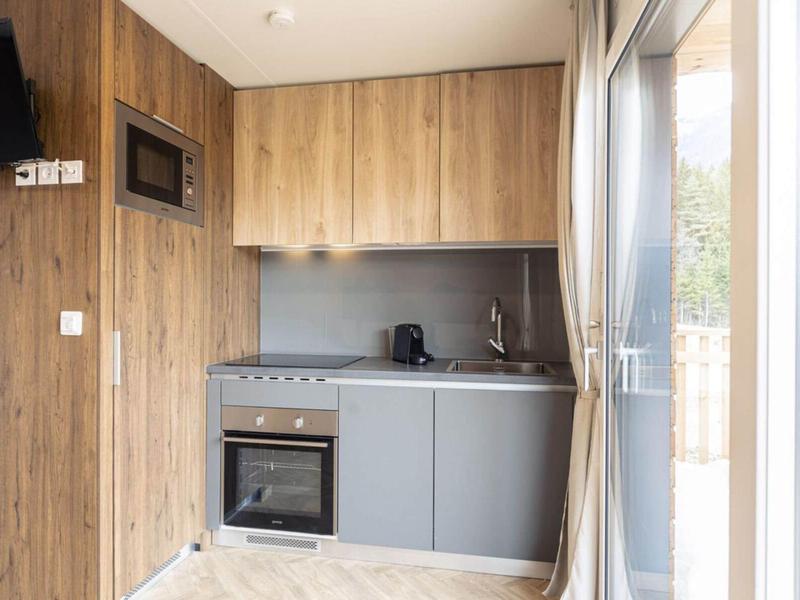 Kleine moderne Küche mit Holzverkleidung, grauen Schränken, Herd, Backofen und großem Fenster mit Vorhang.