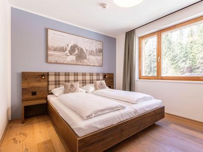 Modernes Schlafzimmer mit Doppelbett, Holzrahmen und großem Fenster mit Waldsicht.