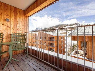 Balkon mit Holzboden und grünen Stühlen, Blick auf verschneite Berge und Gebäude.