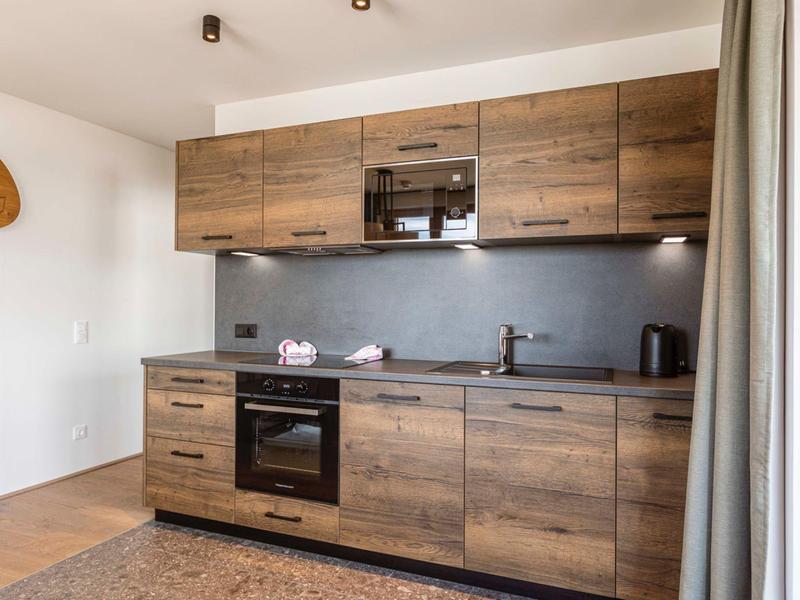 Moderne Küche mit Holzfronten, schwarzen Geräten und weißer Wand, natürlich beleuchtet.