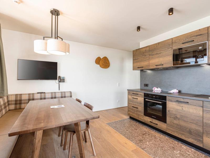 Moderner Essbereich und Küche mit Holzfronten, großem Holztisch, Stühlen und Wand-TV.