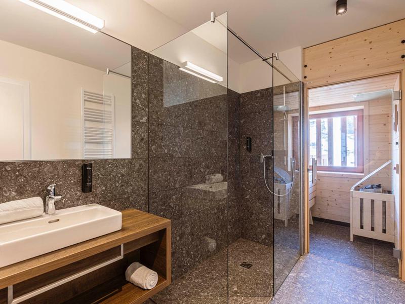 Helles Badezimmer mit Glas-Dusche, weißem Waschbecken, Holzmöbeln und hellem Mosaikfliesenboden.