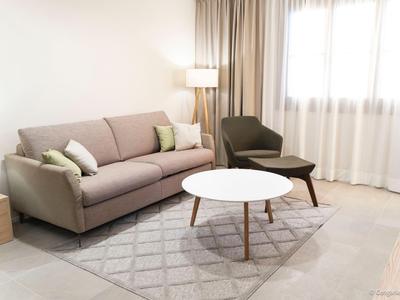 Moderní obývací pokoj s pohovkou, křeslem, kulatým konferenčním stolkem a kobercem před oknem s závěsy.