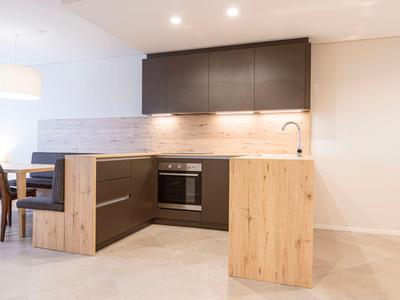 Moderní kuchyň s dřevěnými prvky a tmavými skříňkami v světlé místnosti.