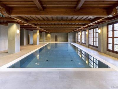 Modern indoor pool with wooden ceiling, large windows, and concrete walls in a hotel.