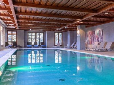 Interior view of a calm indoor pool with wooden ceiling and comfortable lounge chairs.