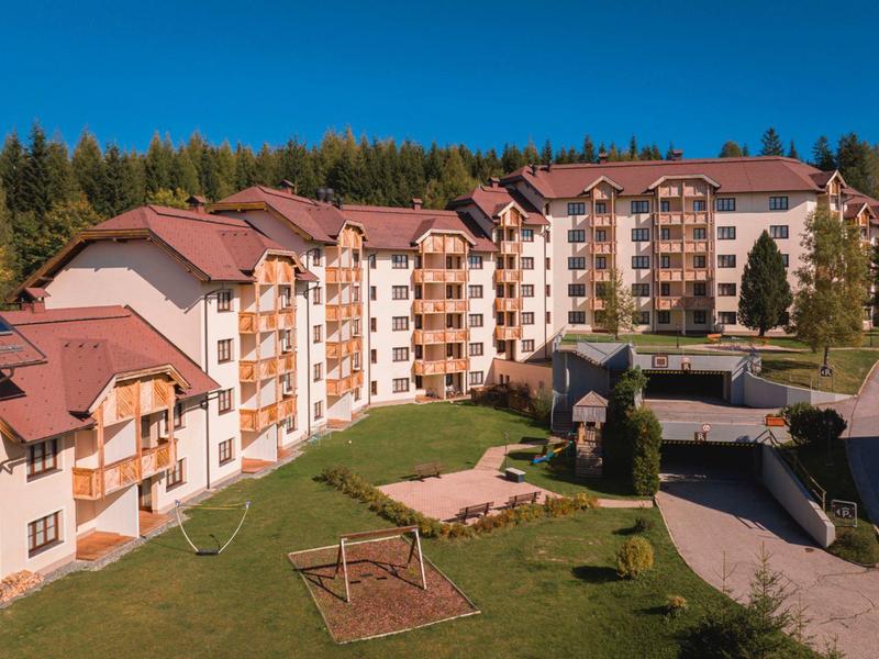 Large hotel building with brown roofs in forested area and playground in foreground.