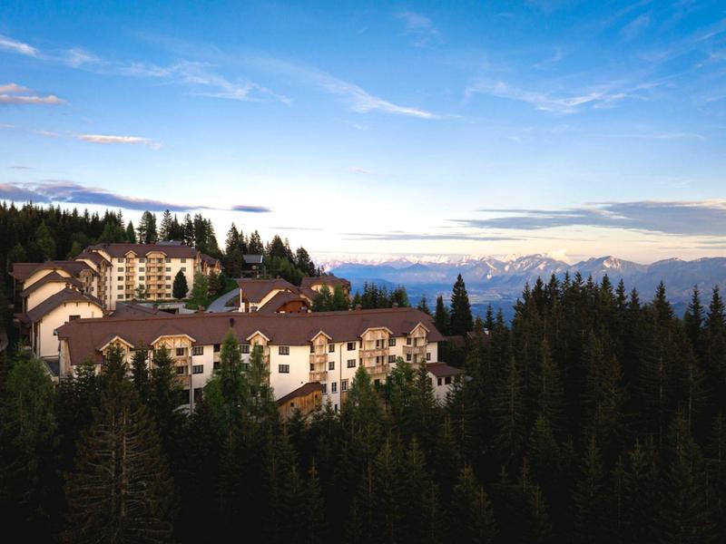 Hotel complex in a forested mountain area with mountains in the background at sunset.