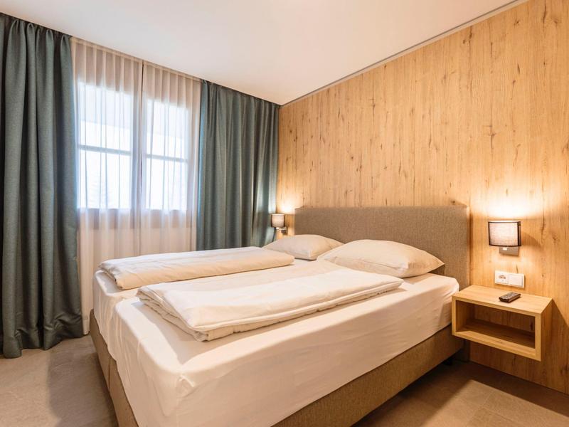 Modern hotel room with two single beds, wood paneling, and natural light.