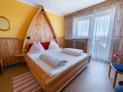 Acogedor dormitorio con muebles de madera, cama grande y ventana con cortina transparente.