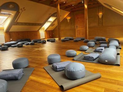 Gran sala tranquila con suelo de madera, cojines de meditación y mantas dobladas sobre colchonetas.