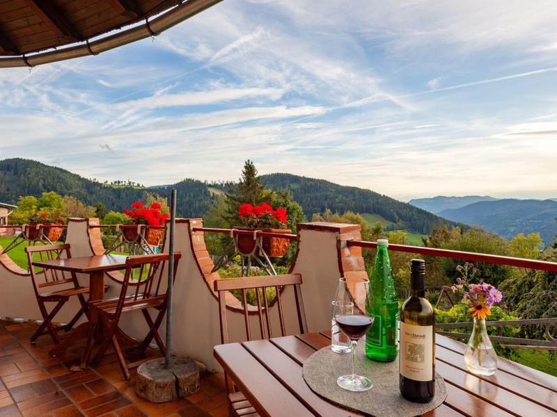 Holzterrasse mit Blumentöpfen, Tischen, Stühlen und Berglandschaft im Hintergrund.