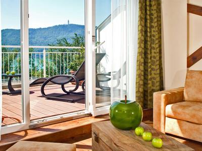Helles Hotelzimmer mit Blick auf Terrasse, Liegestuhl, grüner Vase und Äpfeln auf Holztisch.