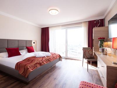 Modernes Hotelzimmer mit Doppelbett, Schreibtisch, Stuhl und Zugang zu Balkon.
