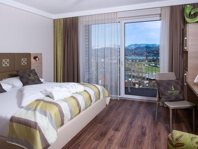Modernes Hotelzimmer mit Doppelbett, Holzboden und Blick auf die Berge durch die Glastür.