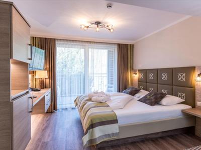 Modern eingerichtetes Hotelzimmer mit Doppelbett, Balkon und hellen Holzmöbeln.