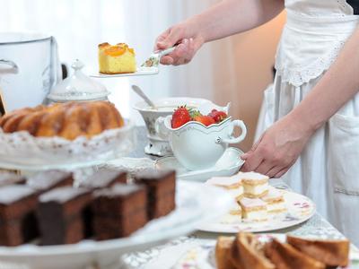 Eine Hand nimmt ein Stück Gebäck von einem dekorierten Tisch mit verschiedenen Kuchen und Tassen.