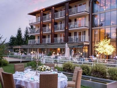 Moderner Hotelkomplex mit beleuchteter Terrasse und gedeckten Tischen im Außenbereich bei Abendlicht.