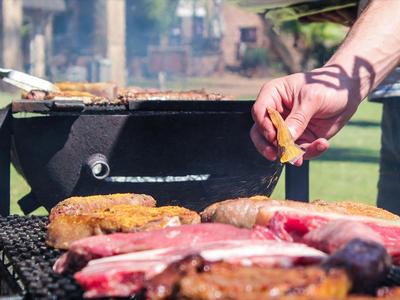 Nahaufnahme von Grillfleisch und Würstchen auf einem Holzkohlegrill im Freien.