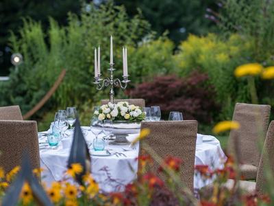 Eleganter gedeckter Tisch im Garten mit Kerzenhalter und Blumenschmuck für ein Hotel-Event.