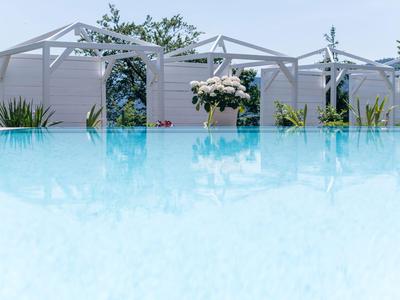 Klares Schwimmbad mit weißen Pergolen und Pflanzen im Hintergrund unter blauem Himmel.