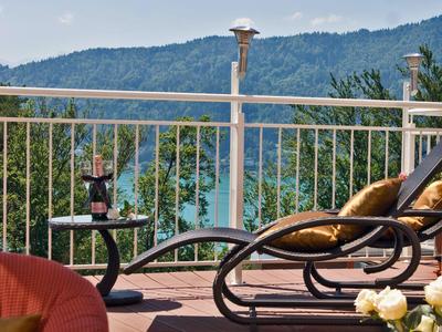 Terrasse mit Liegestühlen, Blick auf Berge und See, bei sonnigem Himmel.