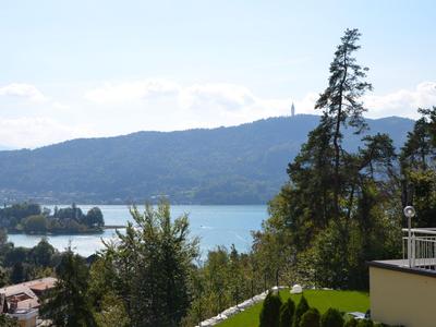 Blick auf einen See mit Hügeln im Hintergrund, Bäume und Hotelterrasse im Vordergrund.