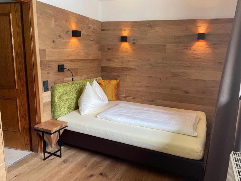 Eenpersoonsbed met wit beddengoed en groene & oranje kussens tegen een houten wand in een hotelkamer.